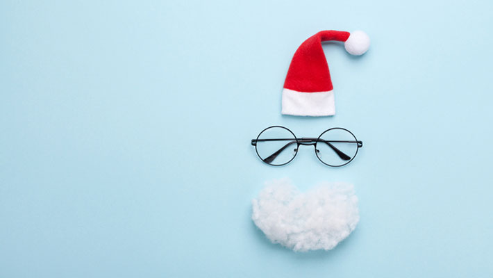 Santa hat, beard and glasses on blue background top view
