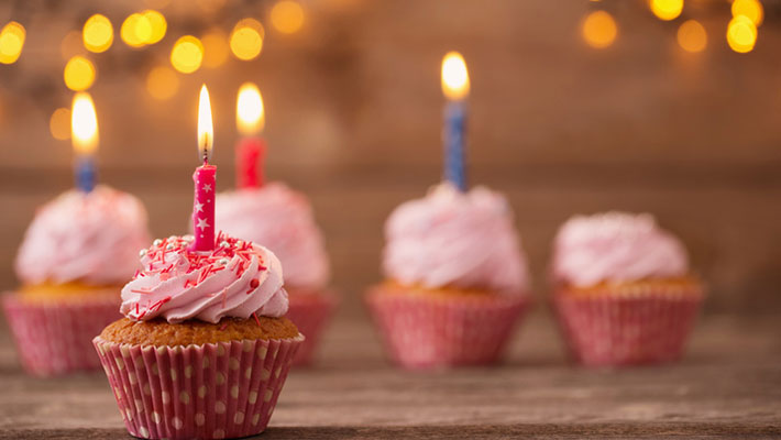 Cupcakes with burning candles on dark old wooden background with lights