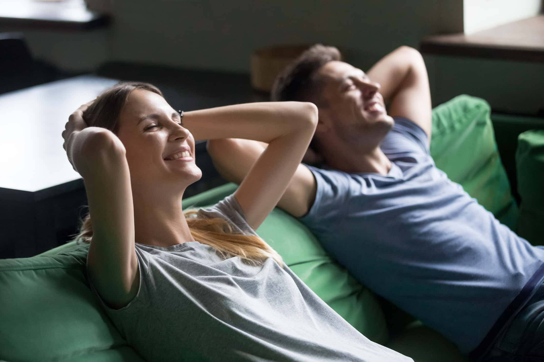 Smiling millennial couple resting on comfortable couch taking break enjoying relaxation or stress relief on free weekend at home