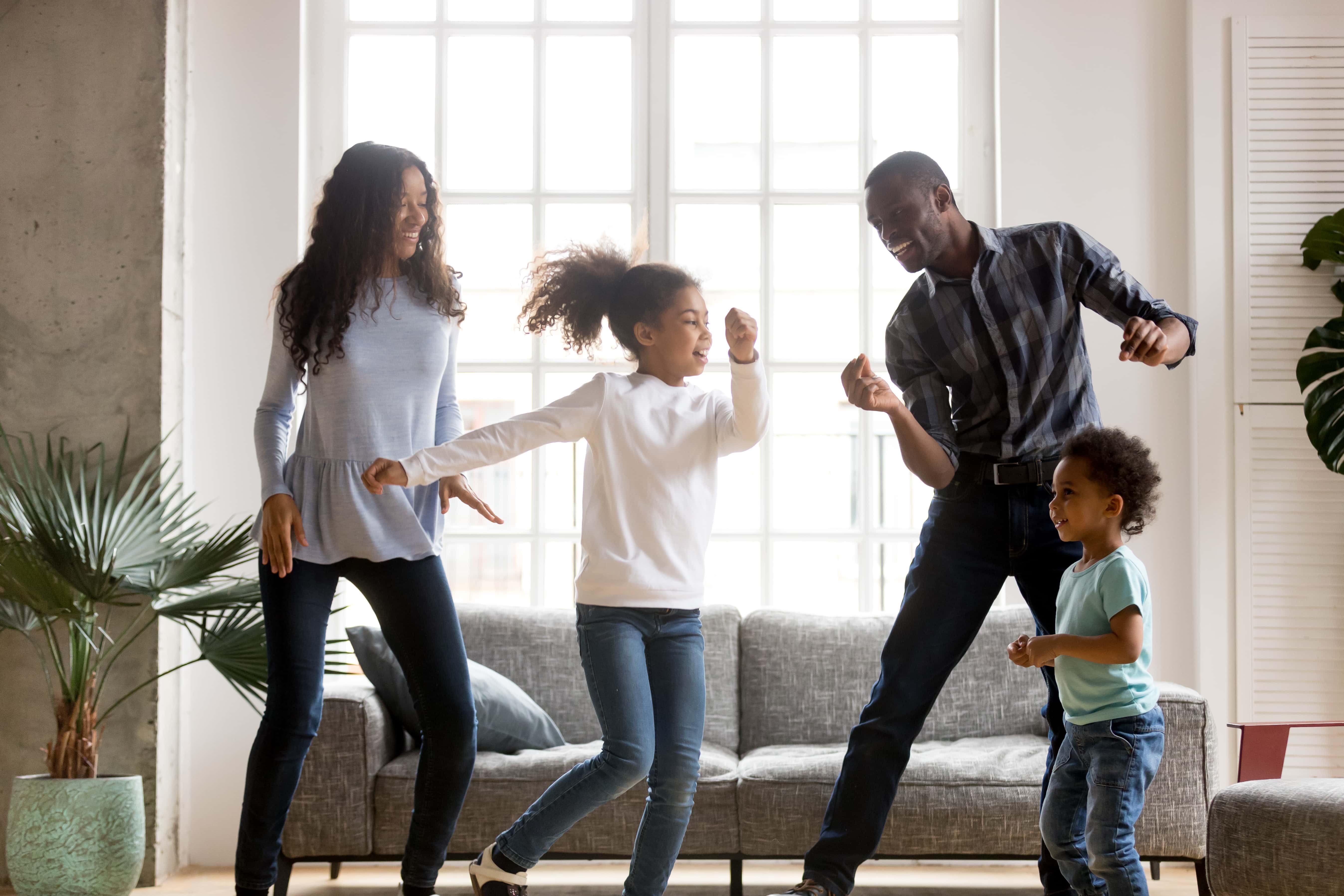 Happy African American family having fun together - mother, daughter, dad, son all dancing.