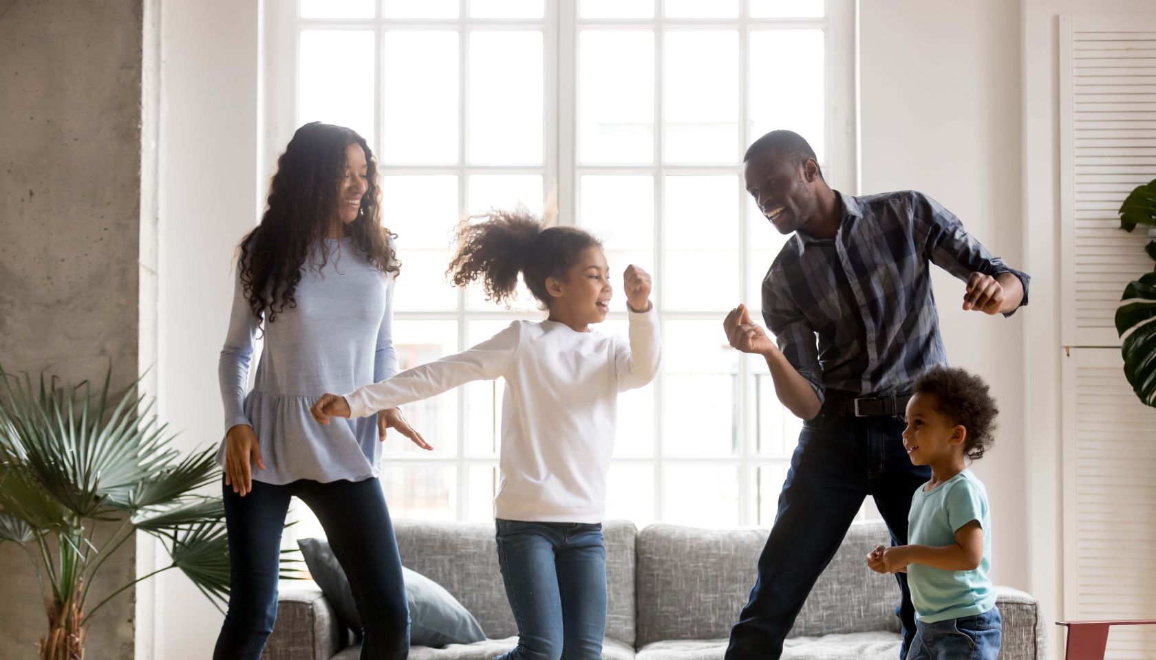 Happy African American family having fun together - mother, daughter, dad, son all dancing.