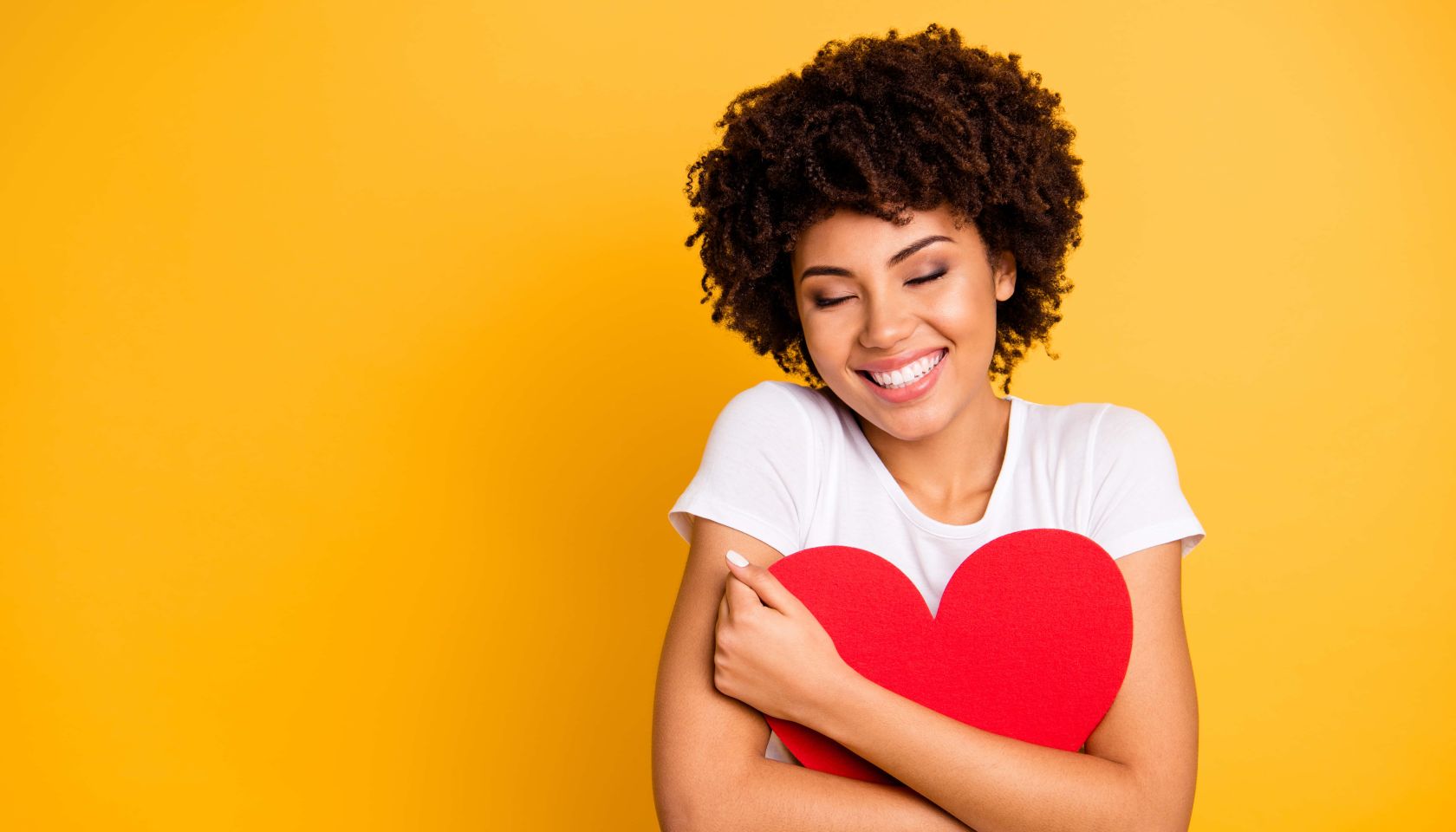 Attractive woman with curly brown hair in a white shirt cuddling big paper card heart shape figure