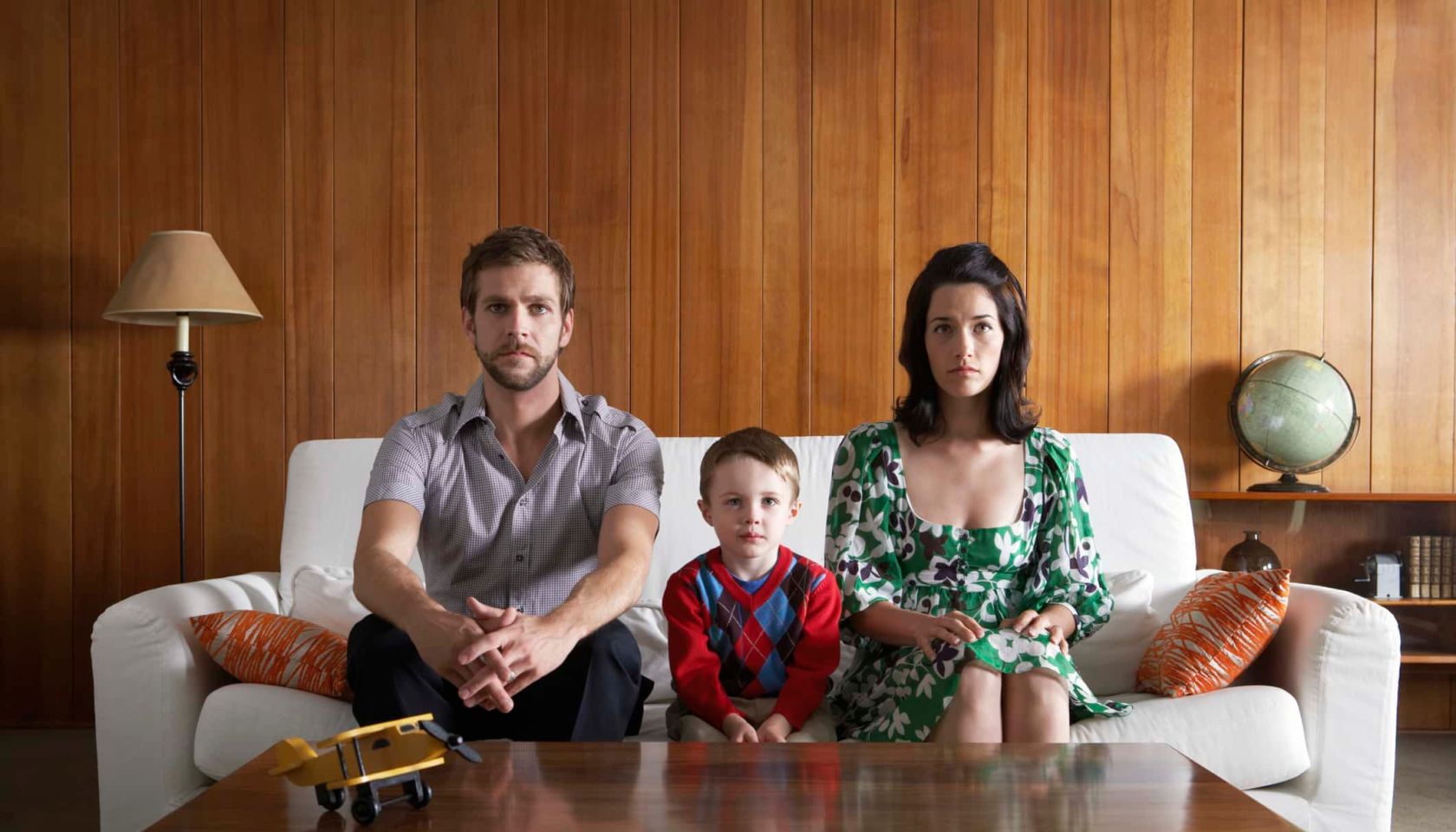 Parents and son (3-5) sitting on couch, in living room - stock photo