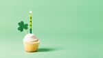 Cupcake with green candle and clover decoration on a green background