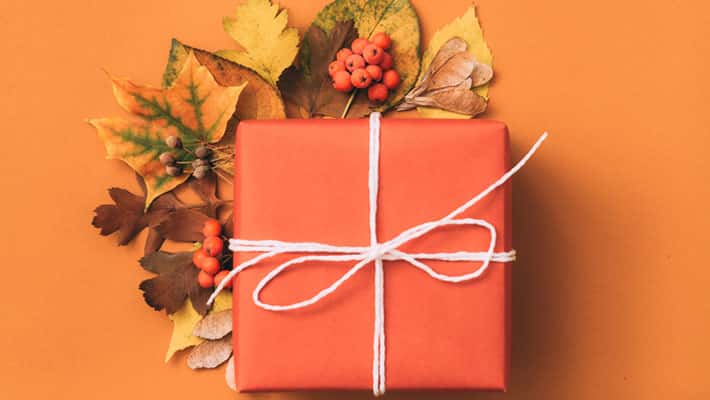 Orange gift box with autumn leaves decor on orange background 