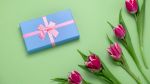 Blue gift box with pink bow and tulips on a green background