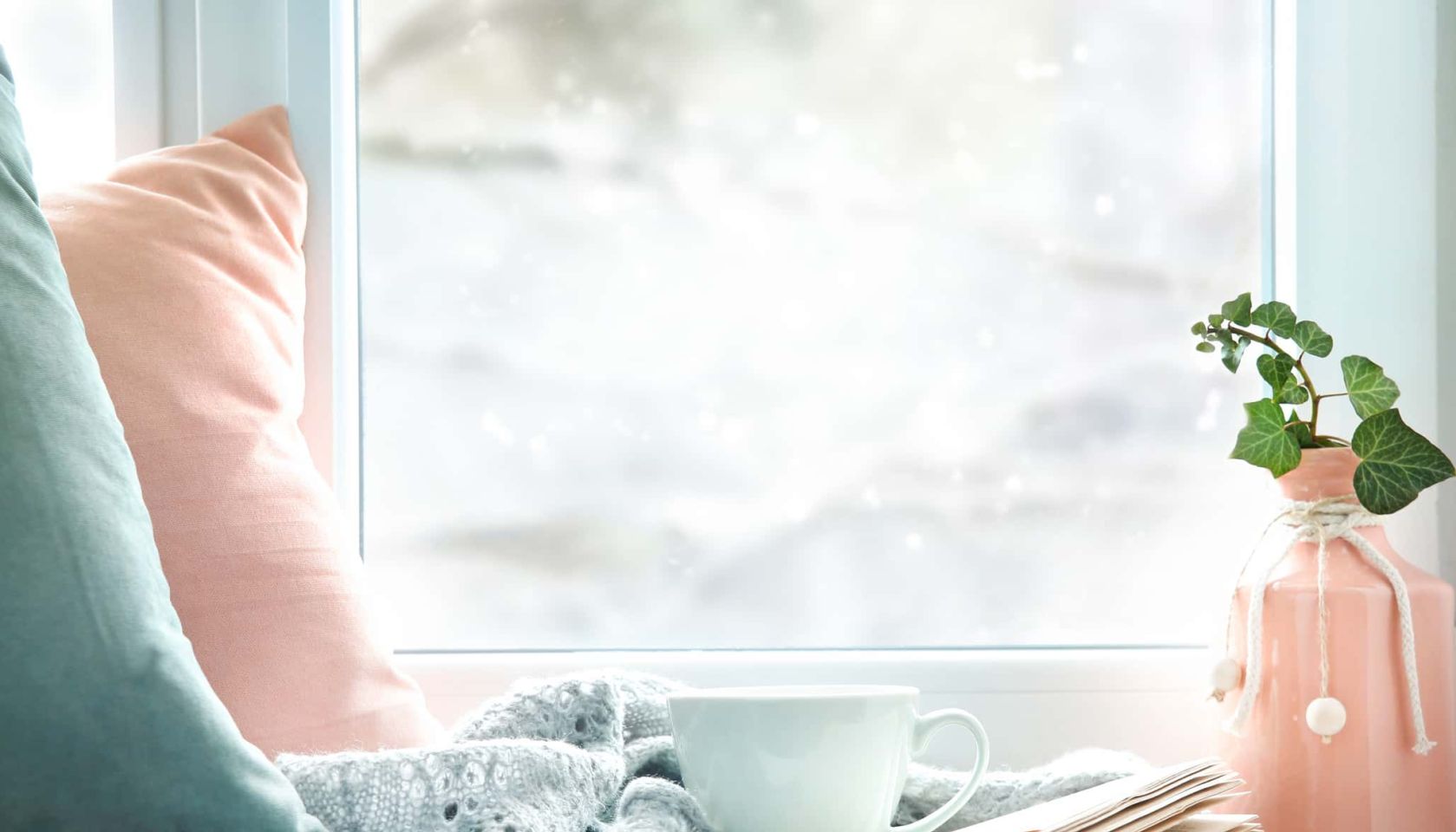 Winter life style background.Mug of tea, book,pillows on window sill empty copy space backdrop.Cold weather mood concept backdrop.