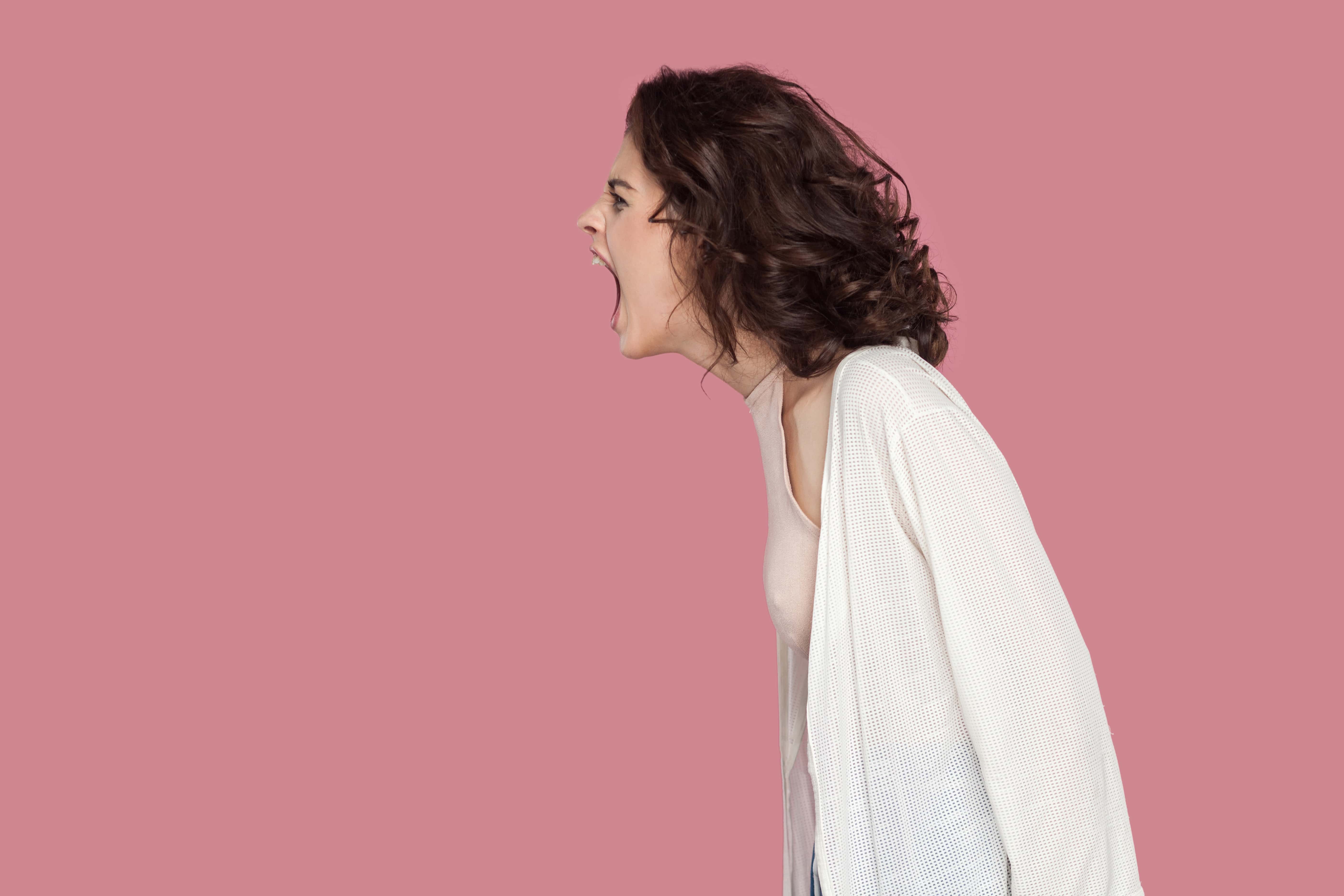 Profile side view portrait of brunette young woman with curly hairstyle in casual style standing and screaming. people expression and emotion.