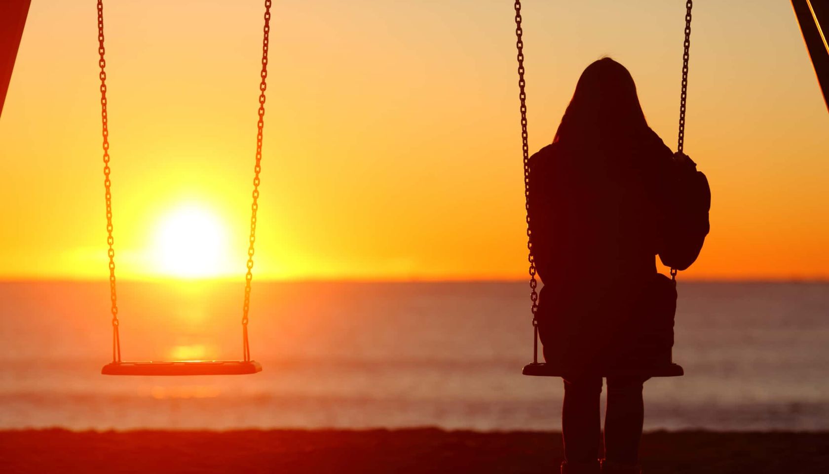 Single woman sitting on a swing contemplating sunset