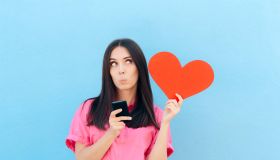 Girl using dating app on her phone while holding a red heart