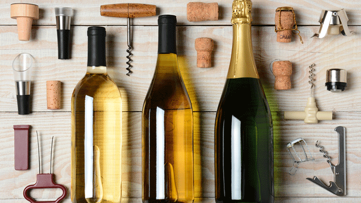 High angle shot of Wine and Champagne bottles surrounded by accessories such as corkscrews, stoppers, pourers and corks. Horizontal format on a rustic white wood table