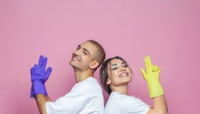 Happy young woman and man ready to clean house on colorful pink background
