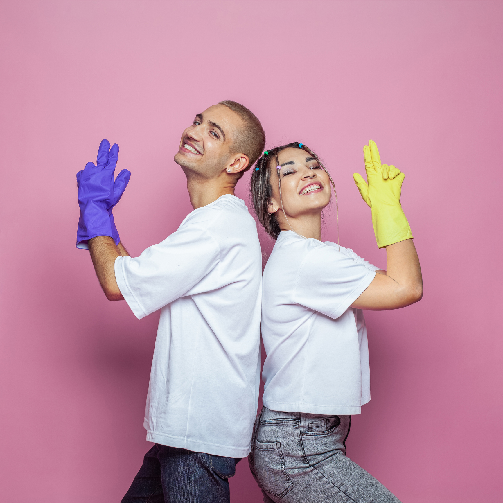 Happy young woman and man ready to clean house on colorful pink background