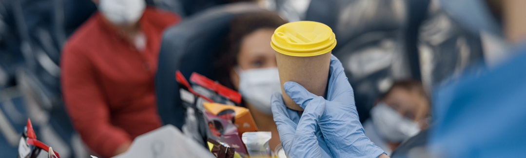 Close up shot of hands in protective gloves of flight attendant serving drinks to passengers on board. Traveling by airplane during Covid19 pandemic