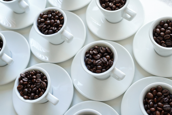 White coffee cups with coffee beans arranged on a white table
