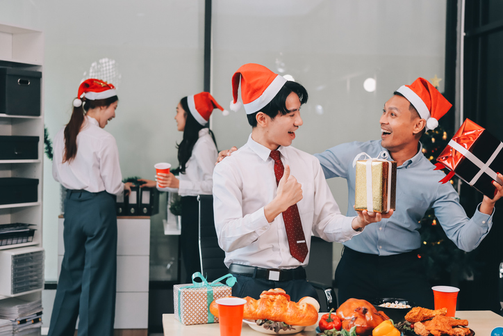 full length view of a group of business team wearing red Santa hat and exchange gift box together in the office for Christmas.