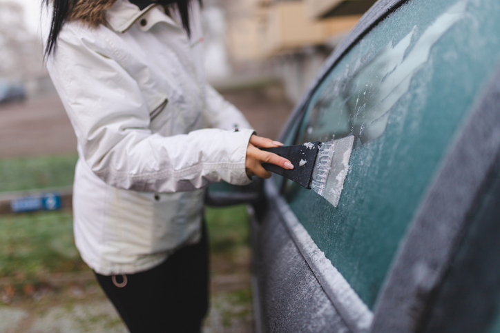 Close-up of a young woman using an ice scrapper to defrost her car's window