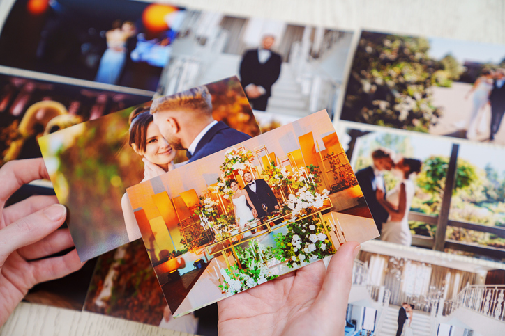 hands with photos and Printed wedding photos laid out on a wooden surface.
