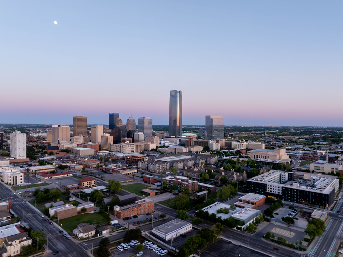 Stunning aerial sunrise view of Oklahoma City skyline with Devon Energy Center standing tall and visible moon, highlighting urban landscape and architectural marvels