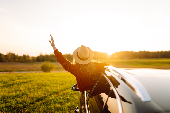 Wanderlust. Happy traveler in hat enjoying car trip leaning out of window.