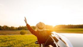 Wanderlust. Happy traveler in hat enjoying car trip leaning out of window.
