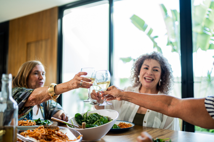 Senior friends women toasting champagne and talking during lunch at home