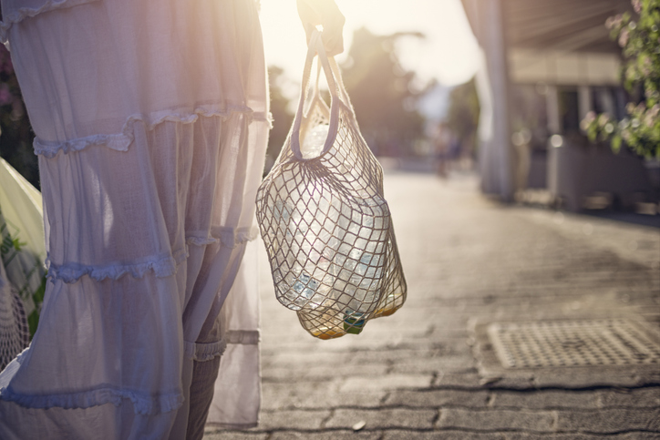 Teenage girl carrying recyclable plastic bottles in a reusable mesh bag outdoors on a sunny day