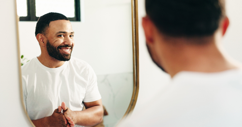 Mirror, beauty and reflection with man in bathroom for skincare, grooming or cosmetics. Morning routine, dermatology progress and facial benefits with person in home for glow, treatment and hydration