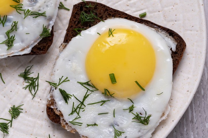 High angle view of delicious fried eggs on dark bread with fresh dill, ready for a healthy breakfast or brunch