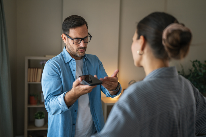 Man showing smart phone to woman during argument