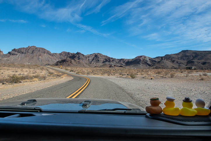 Horizontal color landscape image of southwest desert mountain scenery with bright blue sky and wispy white clouds along the road through the edges of Arizona and California from the passenger POV with Little rubber ducks on the dash watching the road