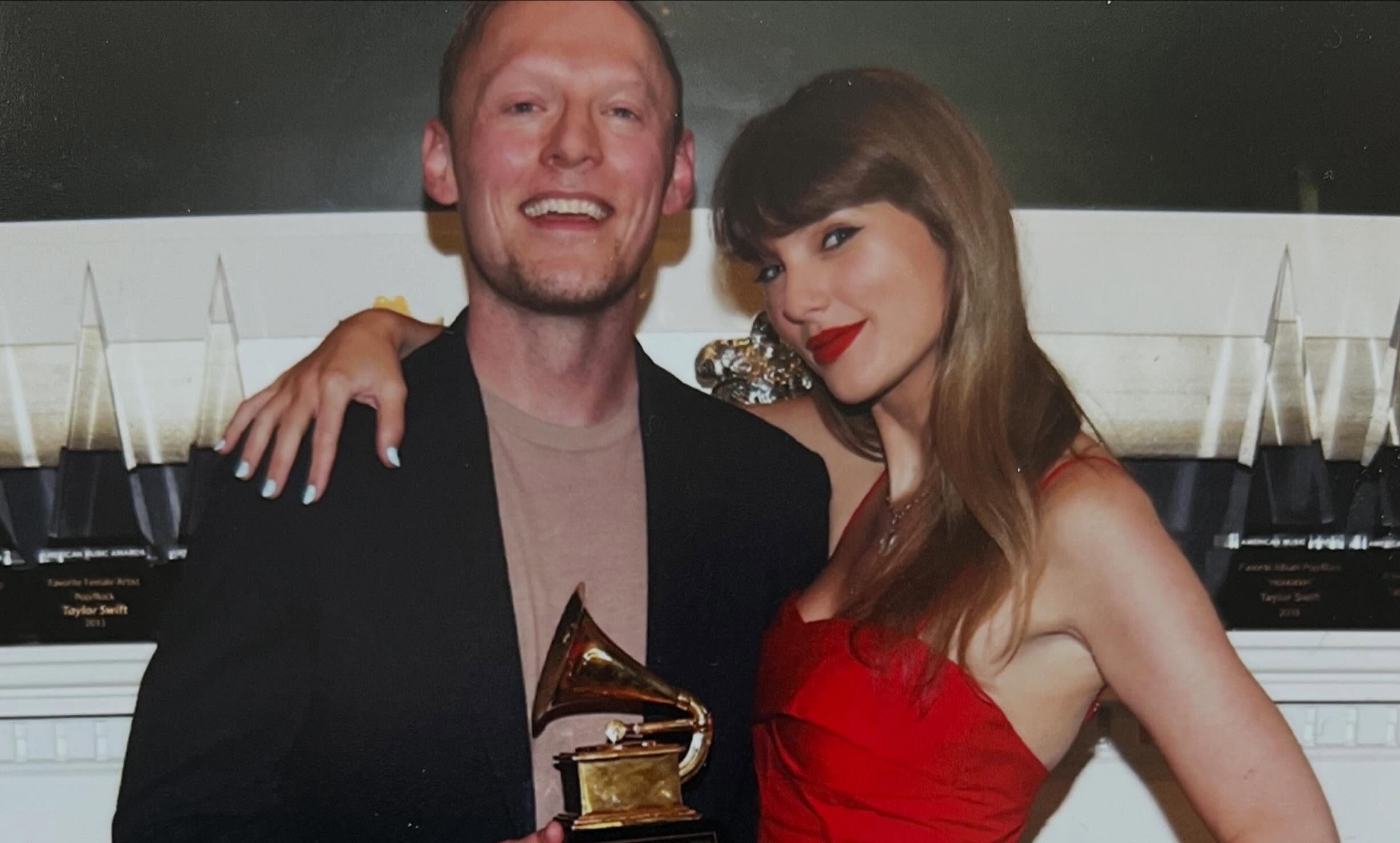 A man in a black suit holds a Grammy award while posing with a woman in a red dress at an awards show.