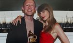 A man in a black suit holds a Grammy award while posing with a woman in a red dress at an awards show.
