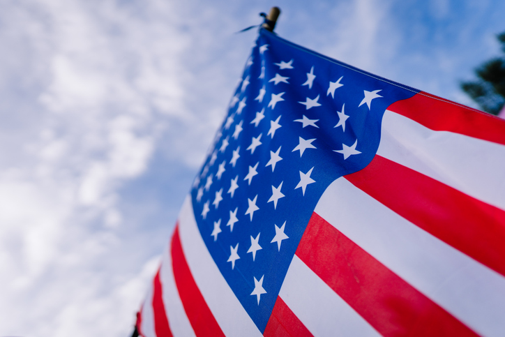 American flag waving against a blue sky with white clouds, showcasing red and white stripes along with blue field of stars, symbolizing patriotism and national pride