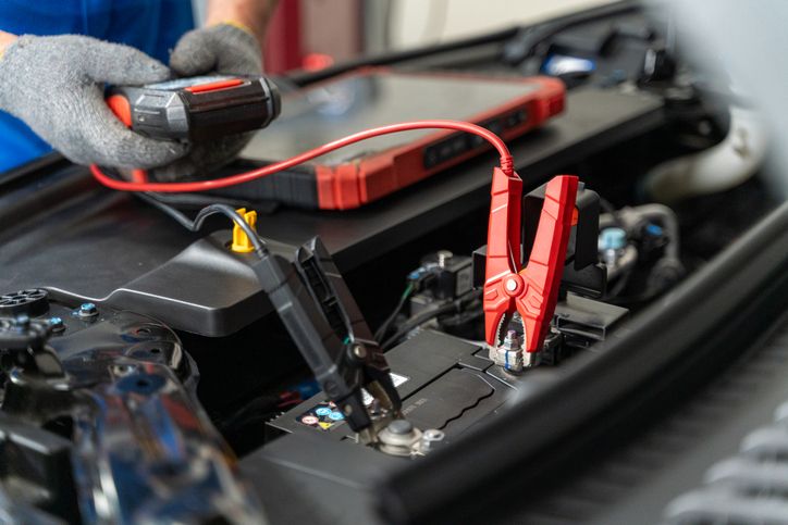 Electric Vehicle Mechanic Testing Car Battery With Jumper Cables