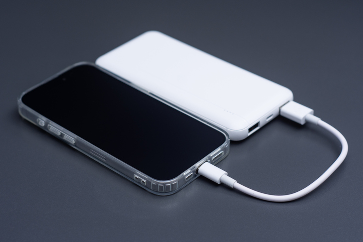 Mobile phone connected to white external power bank with usb cable on dark background. Portable backup battery charging smartphone screen mockup for travel, technology or emergency energy.