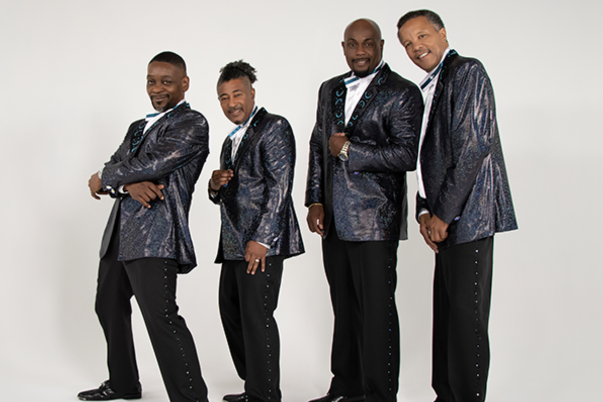 Four well-dressed African American men in matching navy blue and teal suits posing together and smiling.