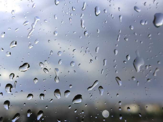 Raindrops on window glass close up with blurred city background during rainy weather.