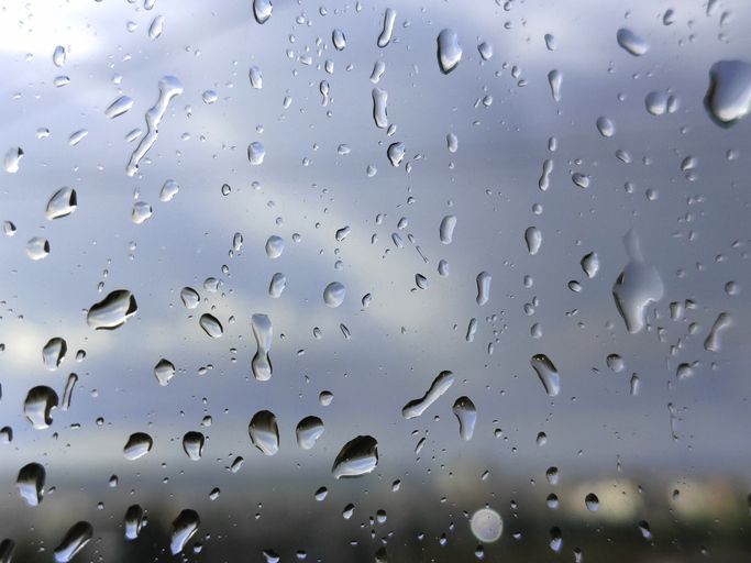 Raindrops on window glass close up with blurred city background during rainy weather.
